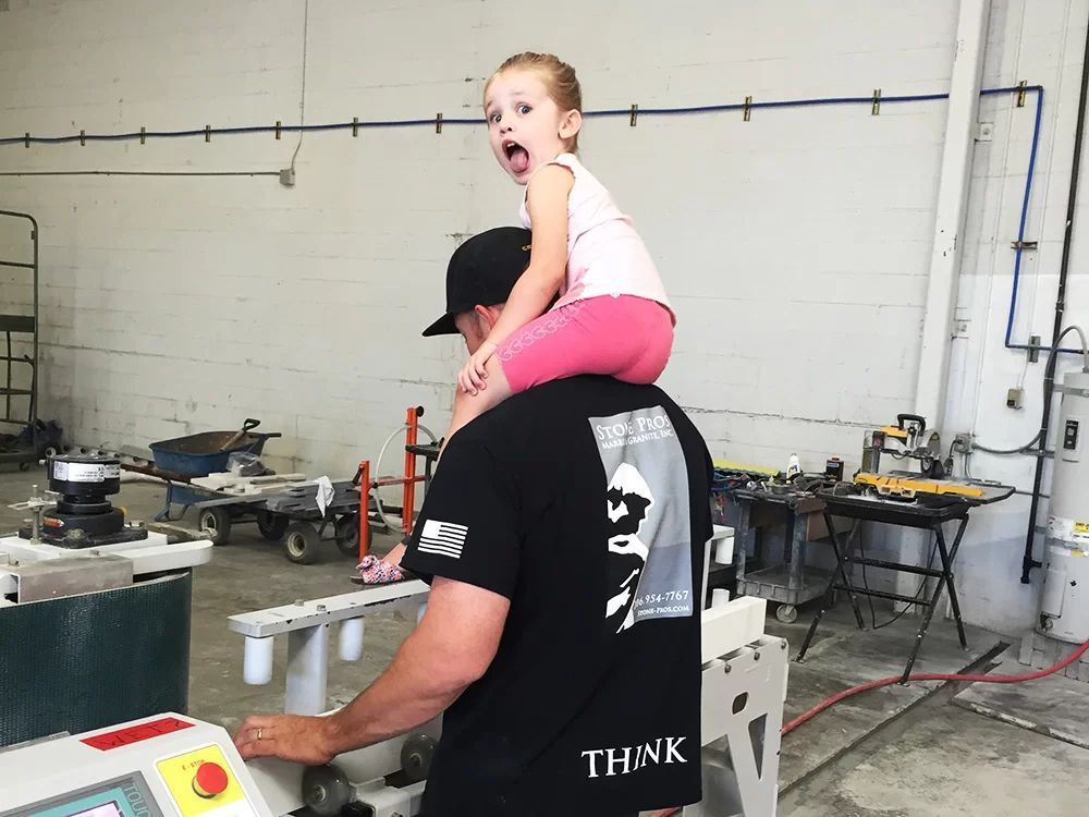 Adult carrying a child on shoulders in a workshop with metal equipment and tools.