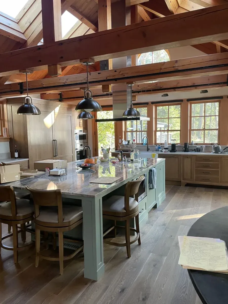 Bright rustic kitchen with wooden beams, mint island, hanging black lamps, and large windows.