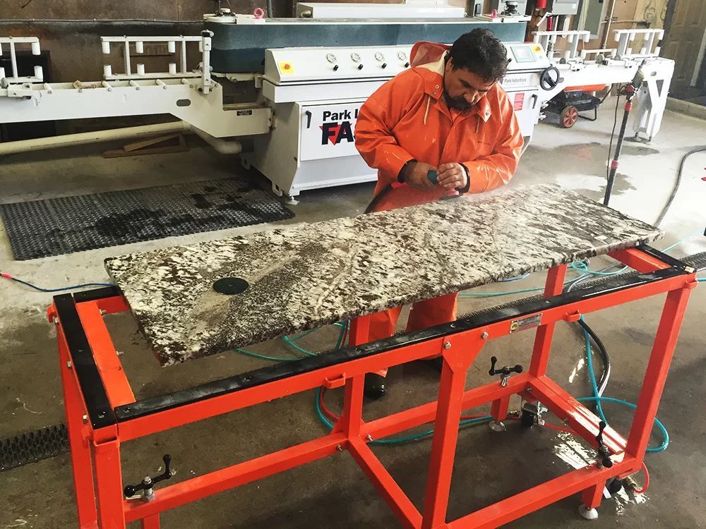 Worker using hand tools on a large stone slab on a red metal workbench in a workshop