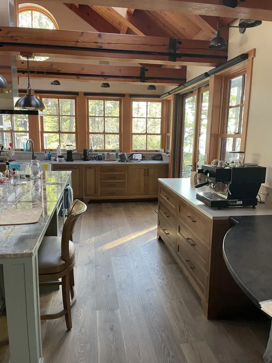 Bright rustic kitchen with wood beams, large windows, and an island with a coffee maker.