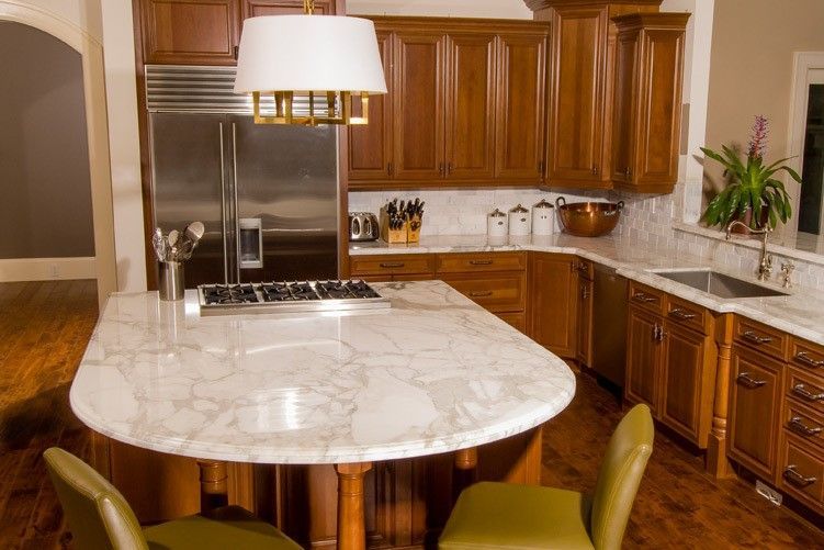 Modern kitchen with marble island, wood cabinets, stainless steel appliances, and pendant lighting.