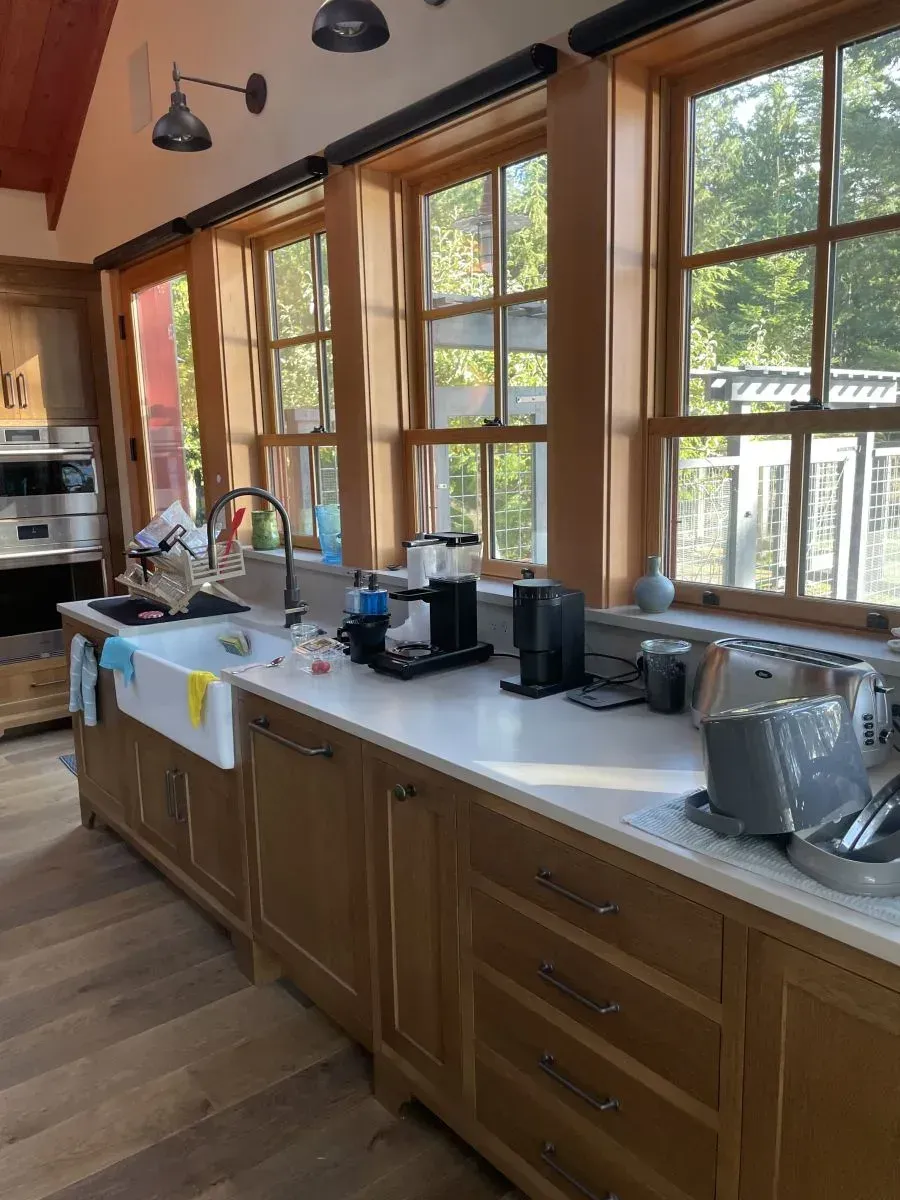 Wood-paneled kitchen with large windows, countertop appliances, and a sink overlooking greenery