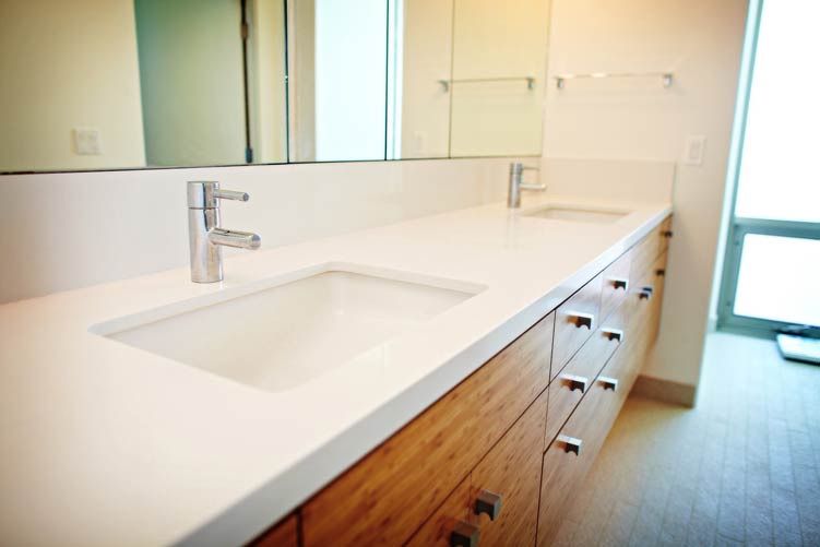 Modern bathroom vanity with white countertop, sink, mirror, and wooden drawers beside a window.