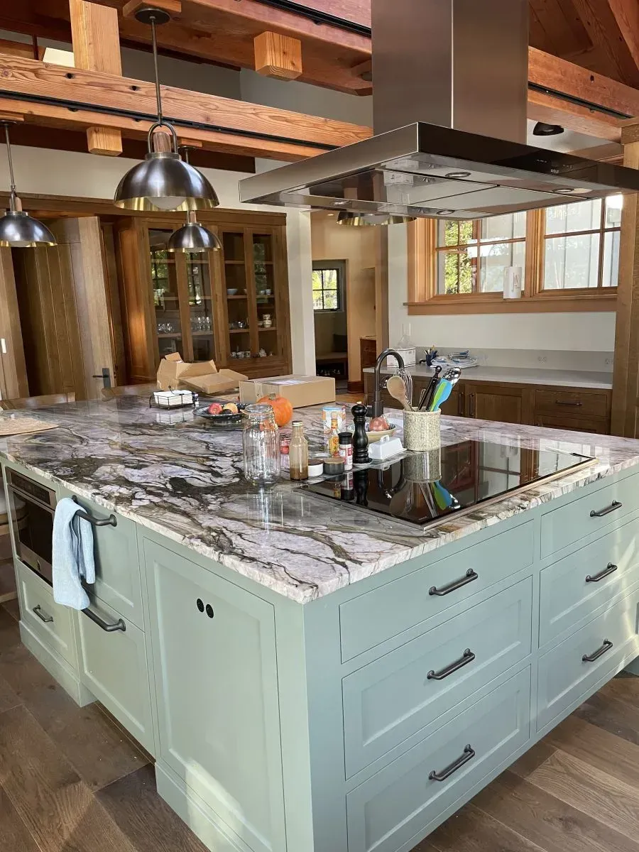 Kitchen island with pale green cabinets, marble countertop, and wood beams in a rustic interior