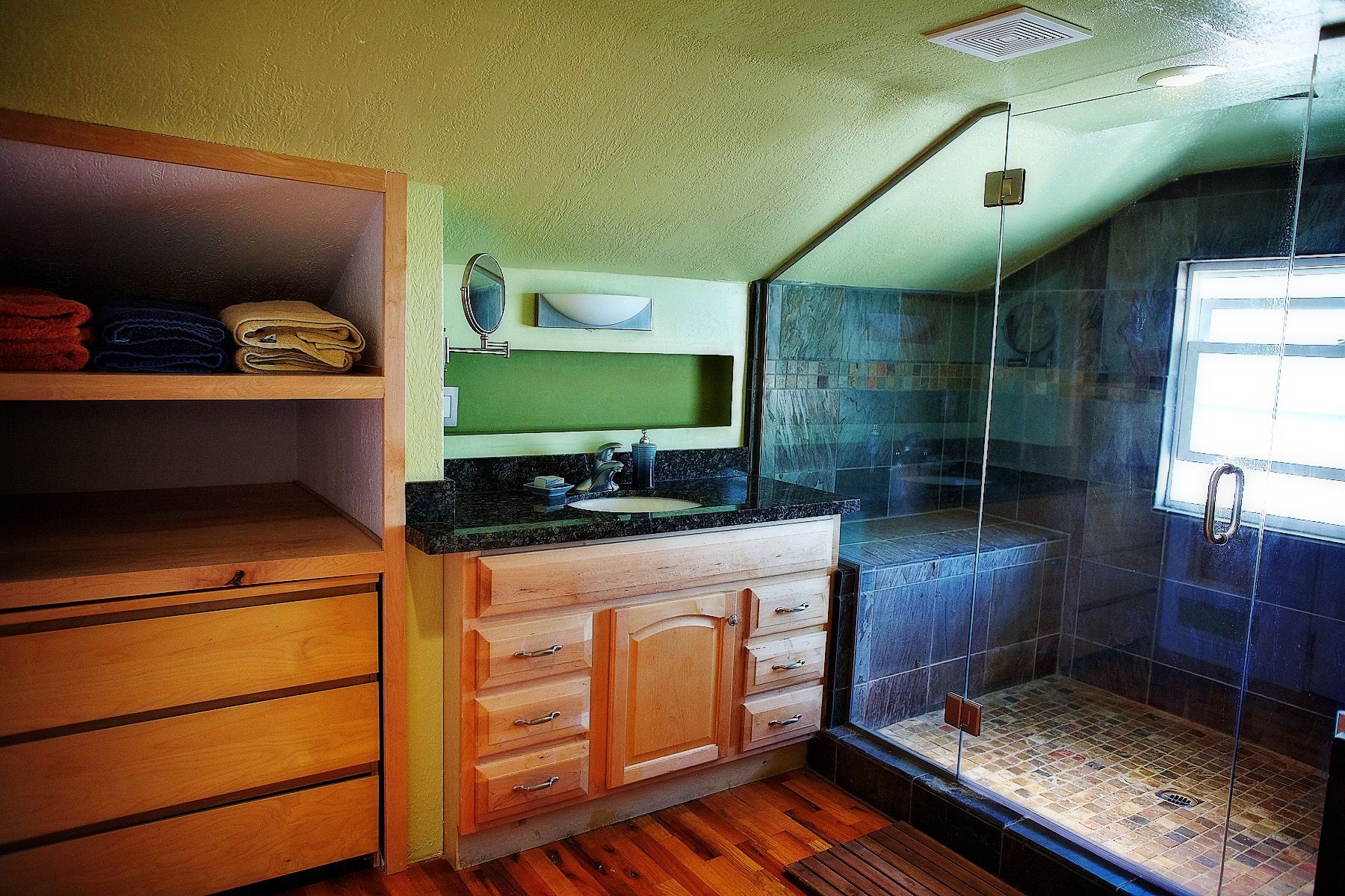Modern bathroom with wood vanity, black countertop, and glass walk-in shower on the right