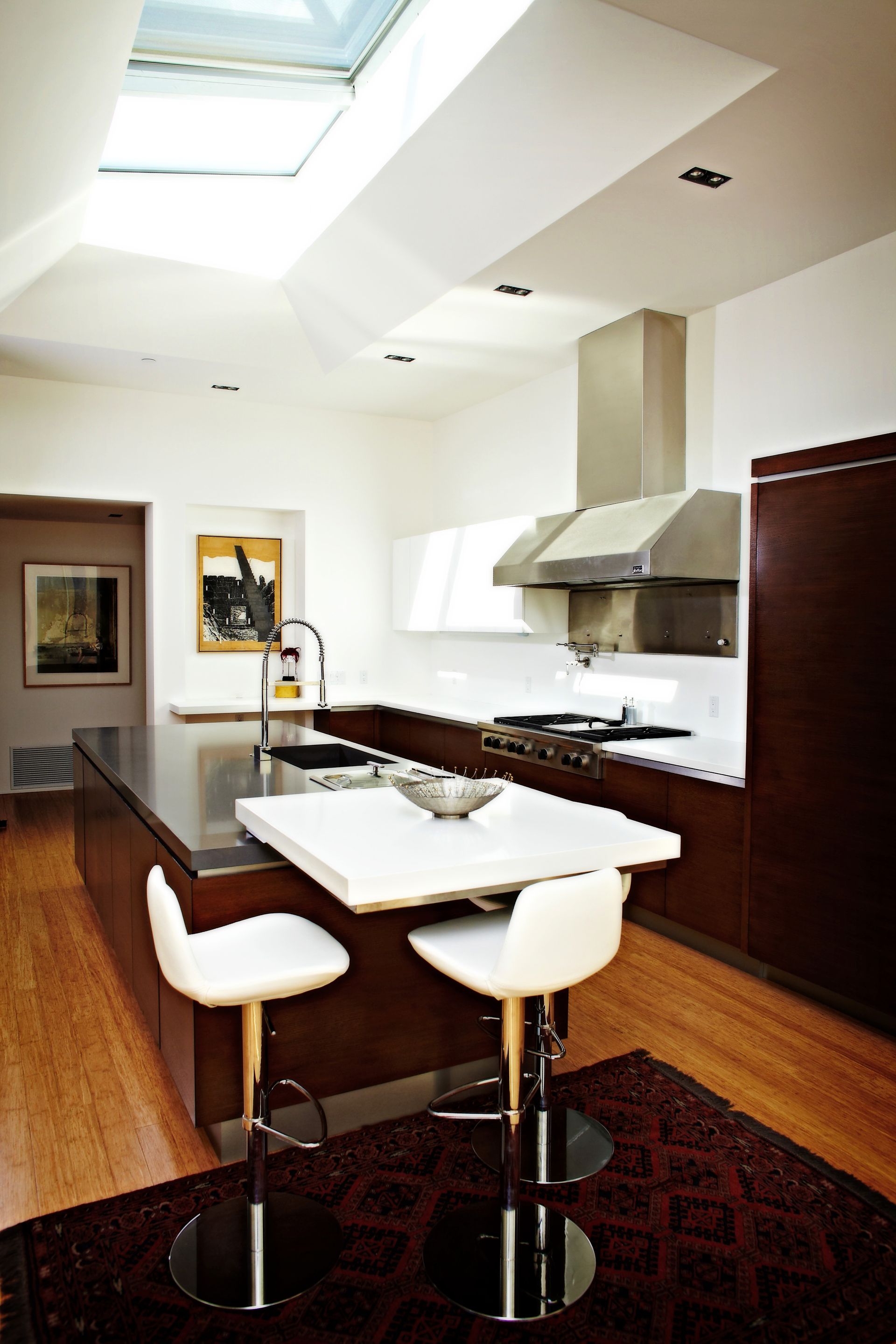 Modern kitchen with island, skylight, white walls, and dark wood flooring