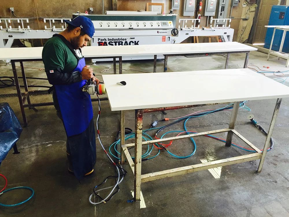 Worker operating machinery in a workshop beside a large white worktable