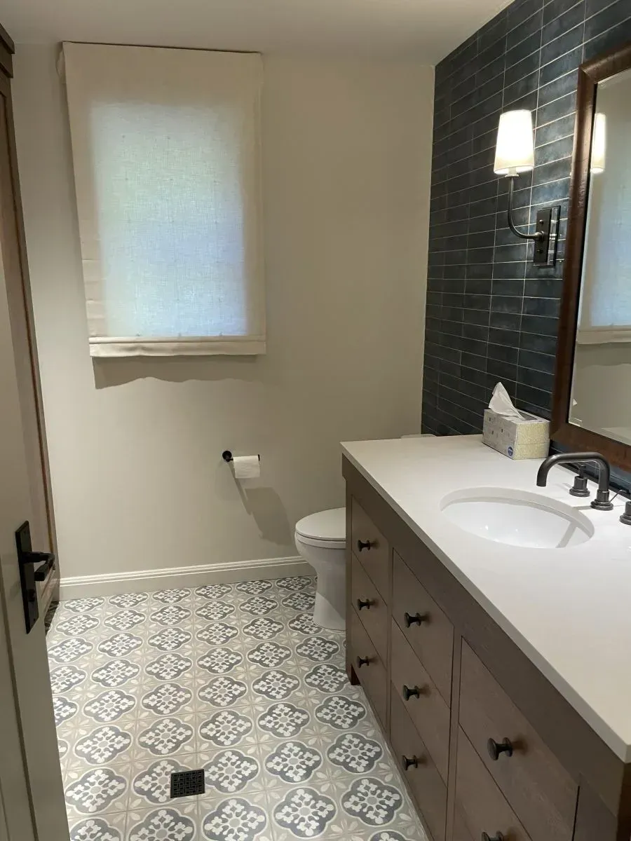 Modern bathroom with white vanity, black tile wall, and patterned floor.