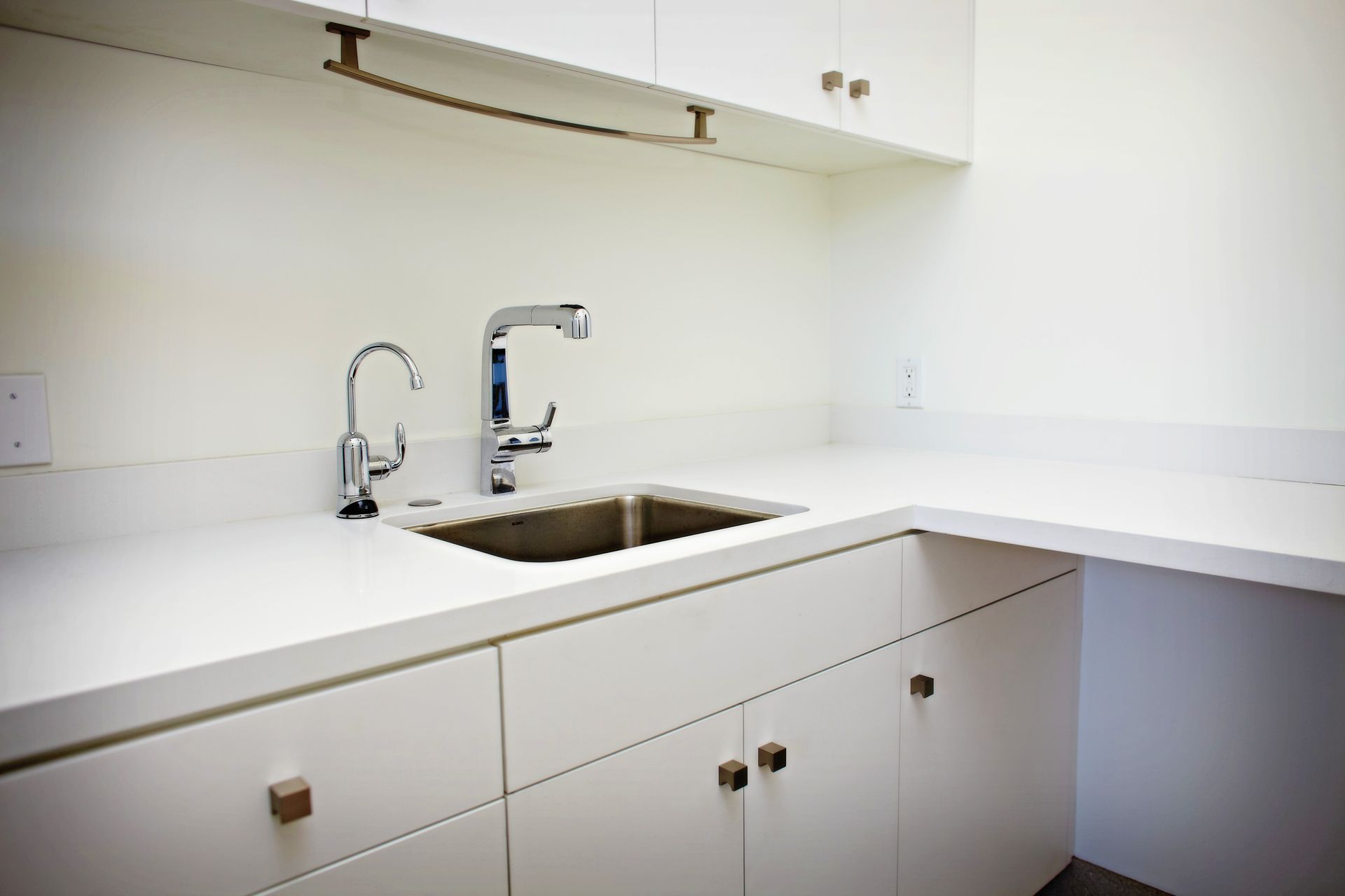 White kitchen countertop with a stainless steel sink and faucet, built-in cabinets, and open shelving