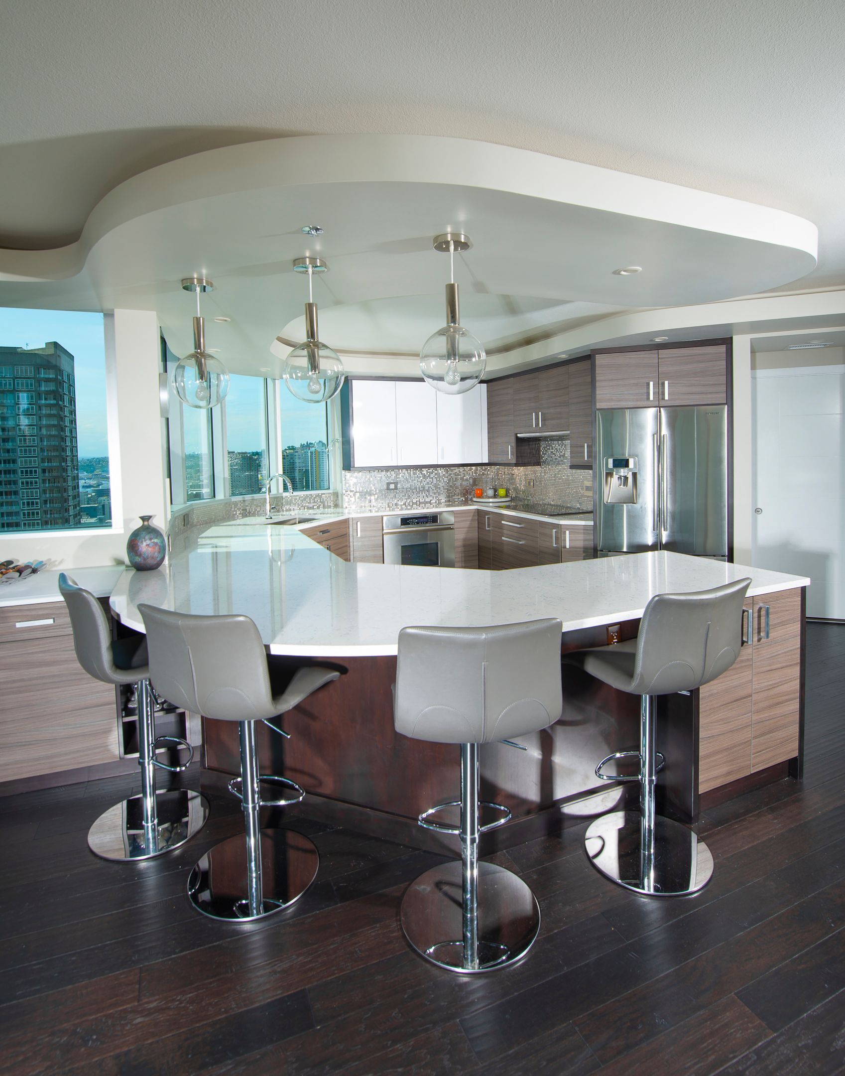 Modern white kitchen with curved island, bar stools, dark wood floor, and stainless steel appliances