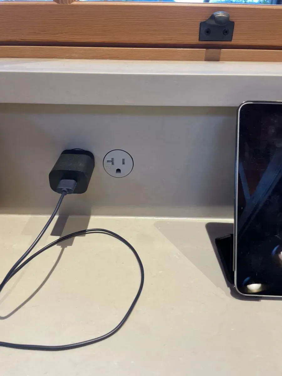 Kitchen countertop with outlet, charging cable, and a smartphone beside a sink.