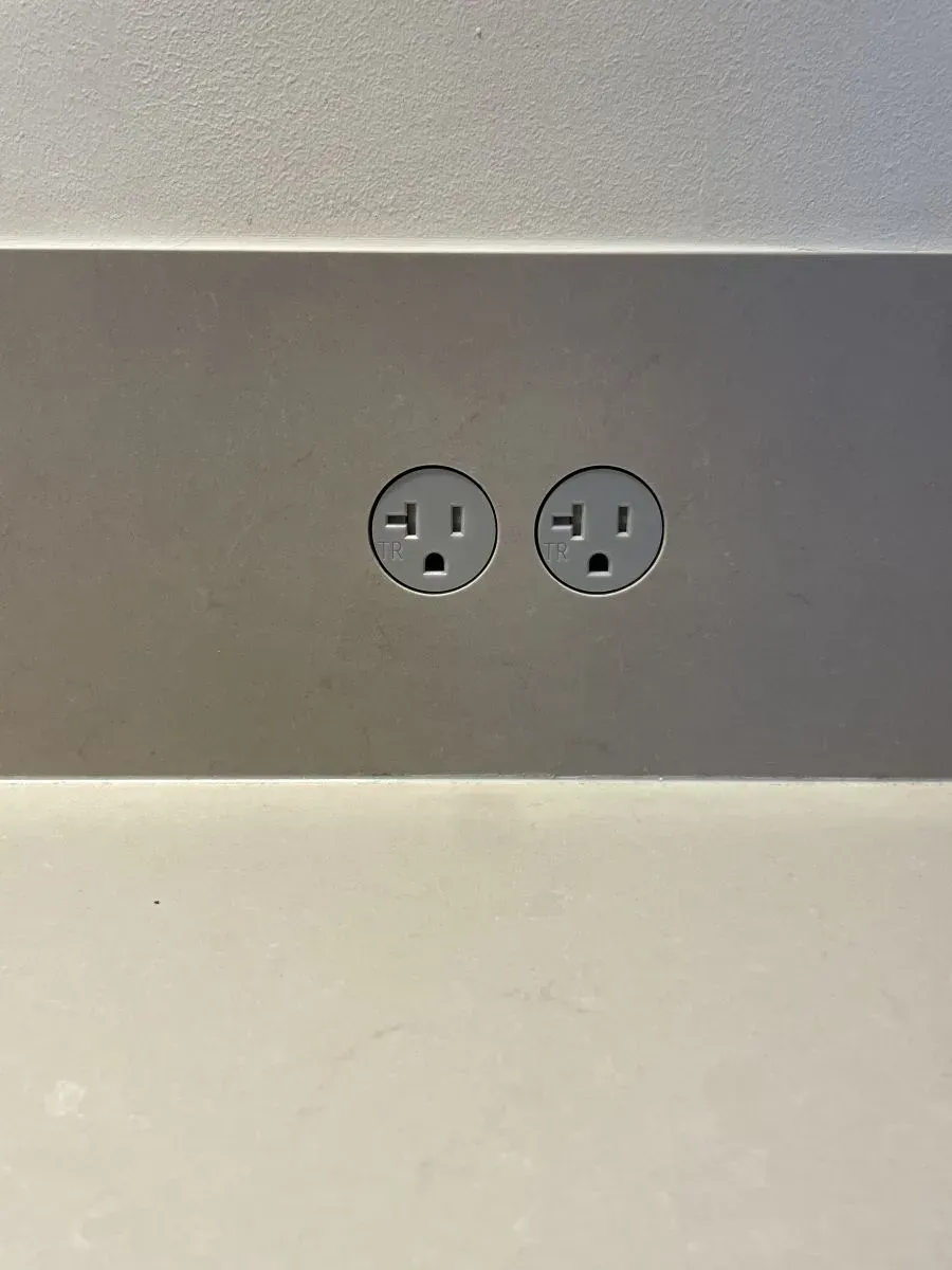 Dual electrical outlets on a brushed metal wall panel above a white surface