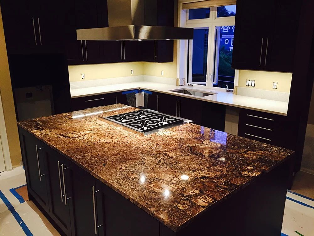 Modern kitchen with a large granite island, dark cabinets, and under-cabinet lighting