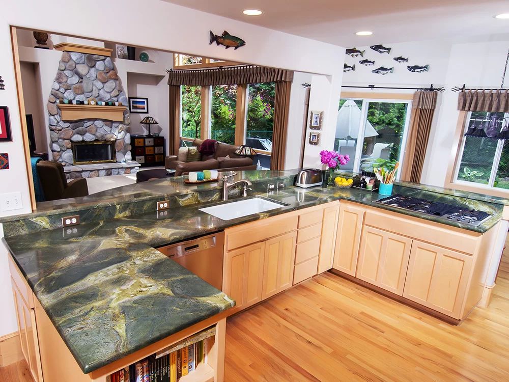 Bright kitchen with green stone countertops, wood cabinets, hardwood floor, and large windows overlooking greenery