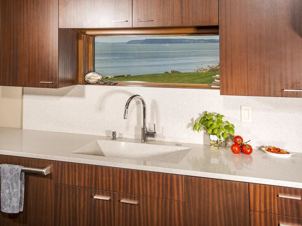 Modern kitchen with wood cabinets, white countertop, sink, and a bay window overlooking water