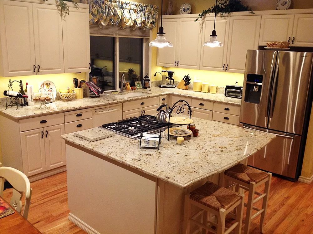 Modern kitchen with granite island, white cabinets, stainless fridge, and warm pendant lighting