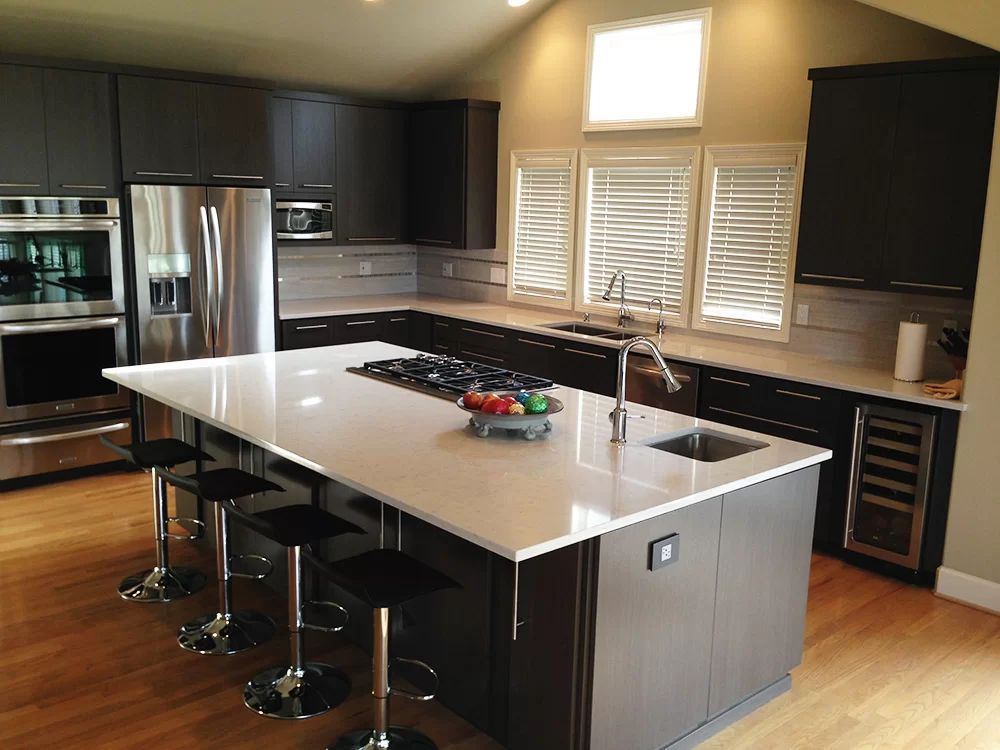 Modern kitchen with dark cabinets, stainless appliances, large island, and stools by the counter.