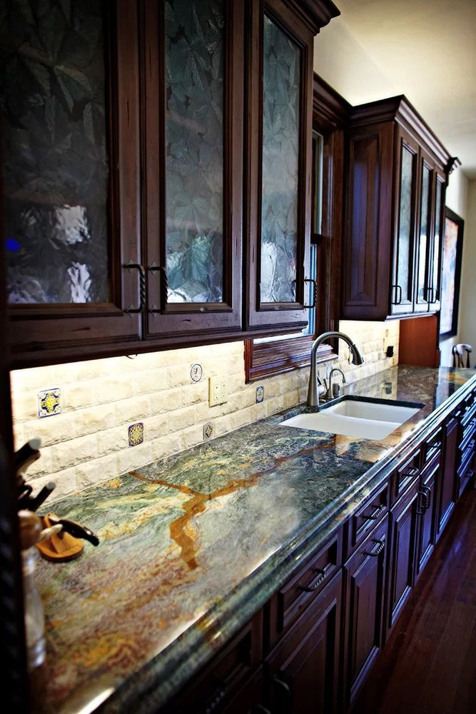 Long kitchen counter with dark wood cabinets and a green marble sink top beside a window