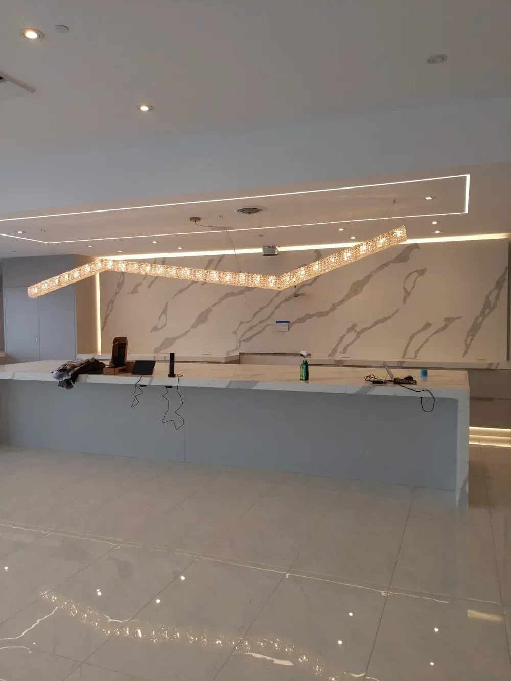 Modern hotel lobby with a marble reception desk, glossy floor, and warm geometric ceiling lights.