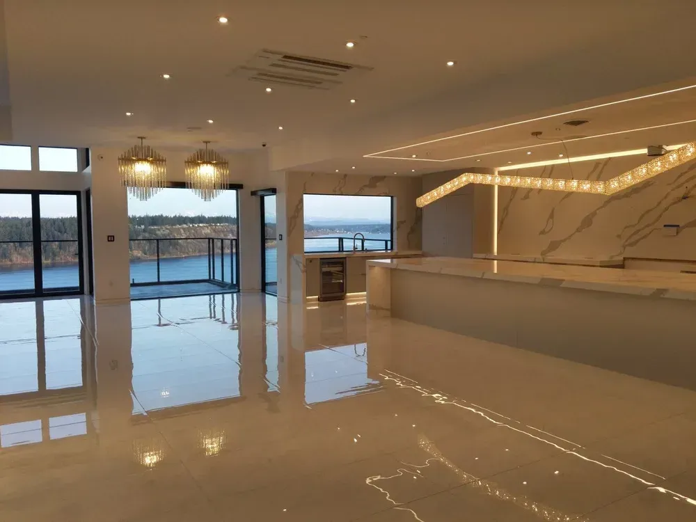 Empty modern lobby with glossy floors, hanging lights, and floor-to-ceiling windows overlooking water at sunset