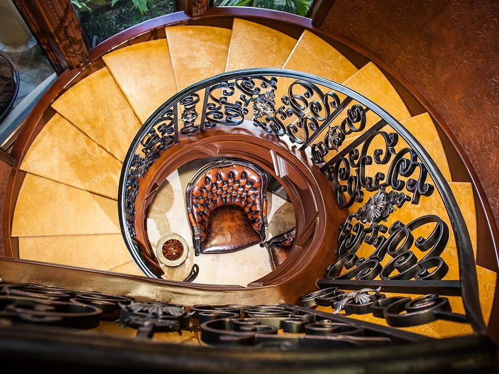 Spiral staircase with ornate black iron railing and warm yellow steps, viewed from above.