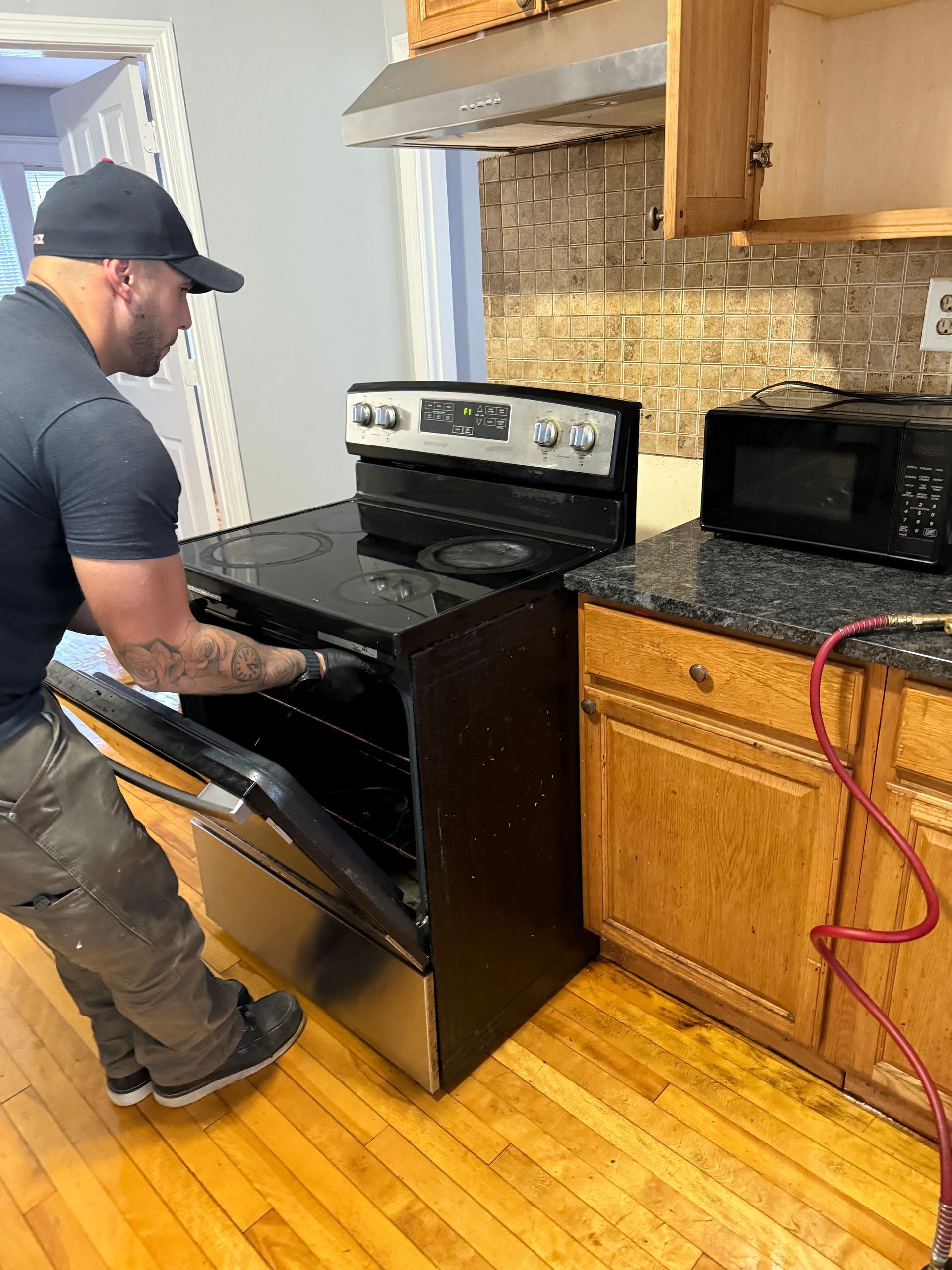 Person installing a black electric range in a kitchen. Open oven door; cabinets and microwave visible.