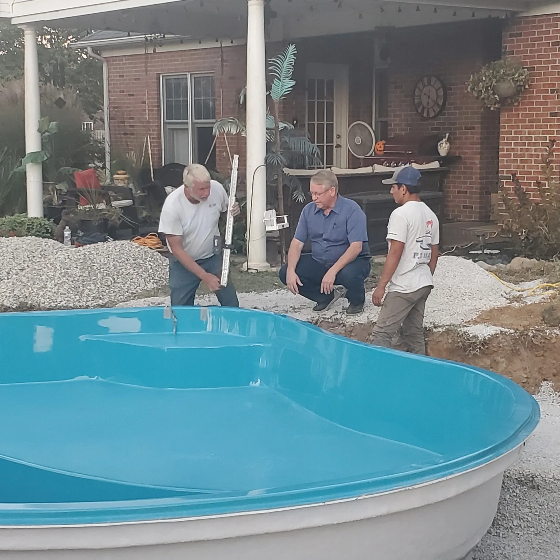 Three men are standing around a large blue swimming pool
