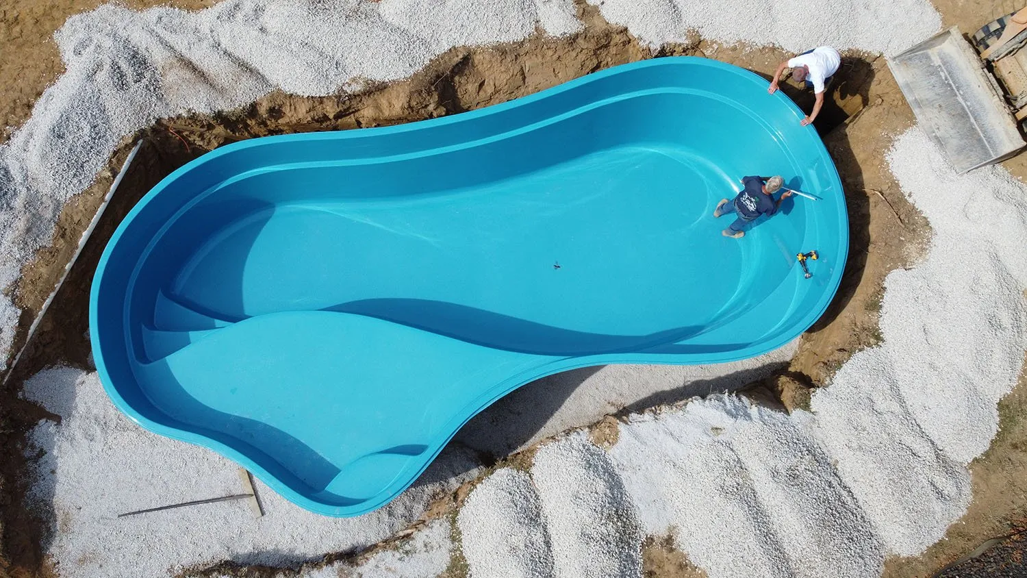 A blue swimming pool is being built in the dirt.