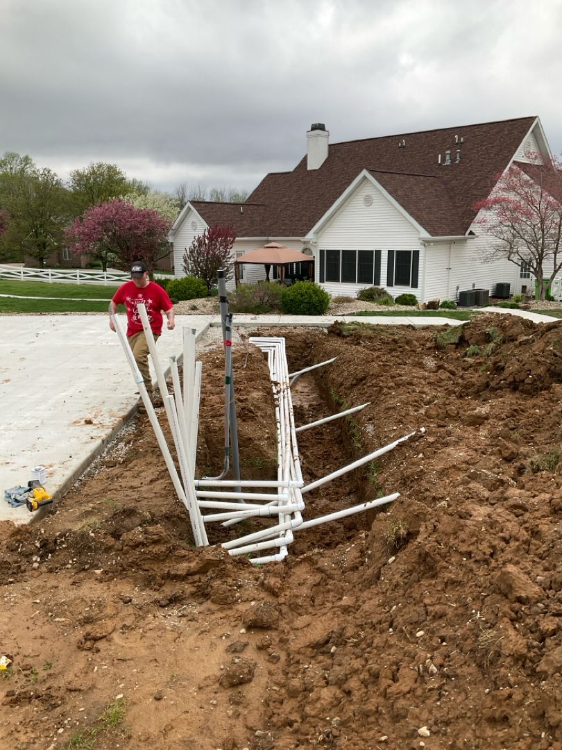 A man is digging a hole in the dirt in front of a house.