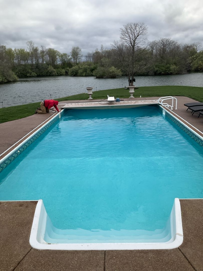 A man is working on the side of a large swimming pool.