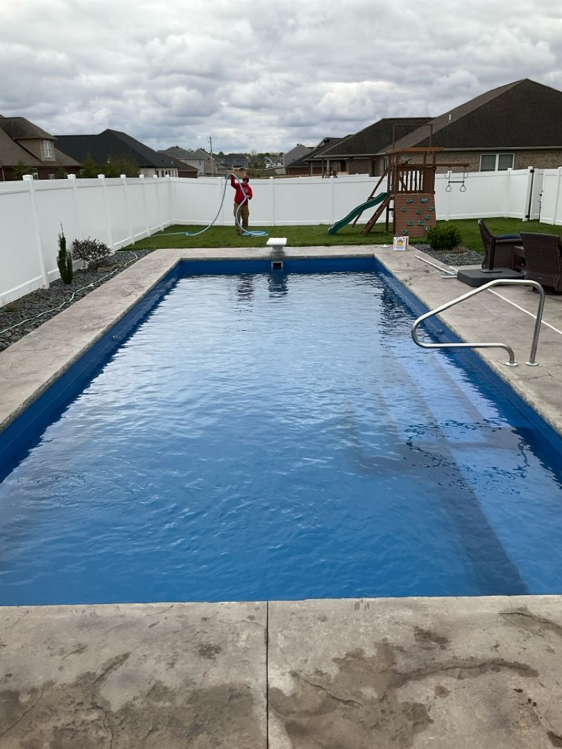 A man is cleaning a large swimming pool in a backyard.