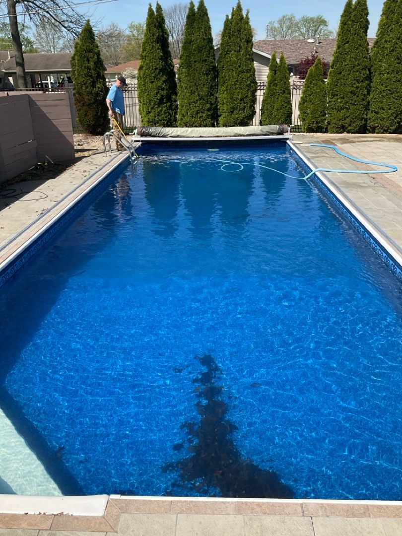 A man is standing next to a large swimming pool surrounded by trees.