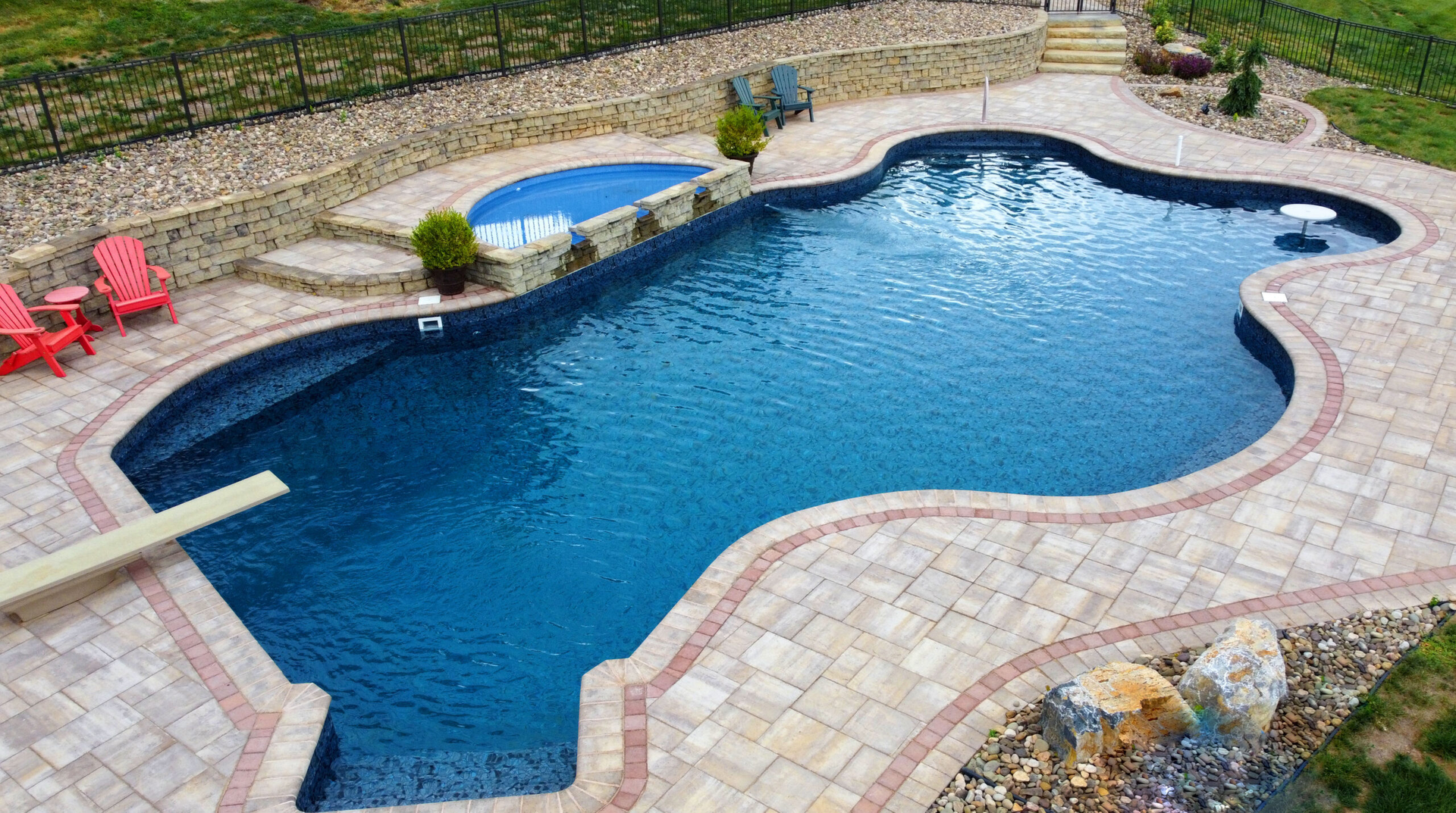 A large swimming pool is surrounded by a brick patio and chairs.