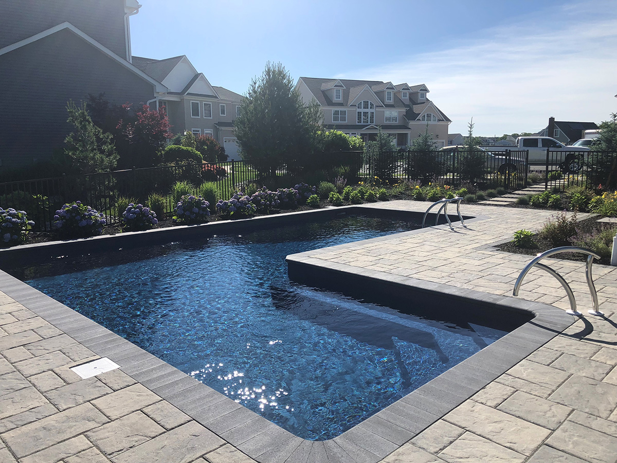 A large swimming pool is surrounded by a brick patio.