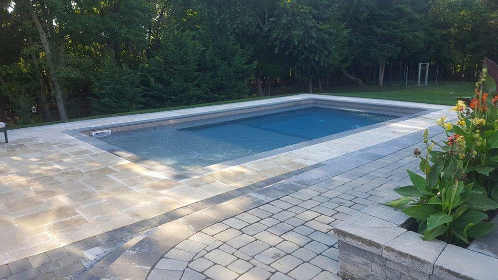 There is a large swimming pool in the backyard surrounded by trees.