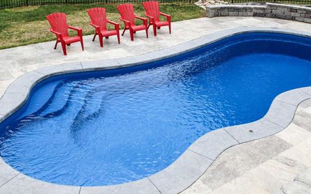 Four red chairs are sitting next to a large blue swimming pool.