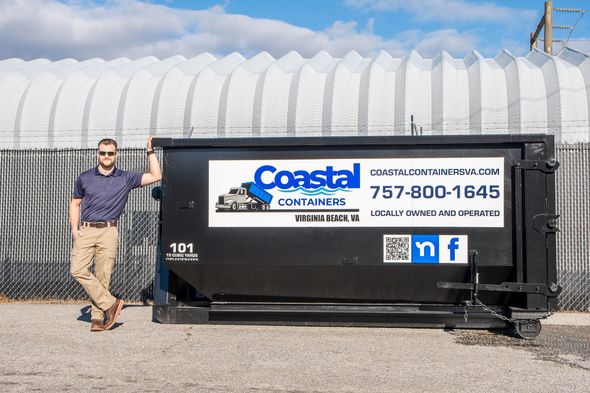 A man is standing next to a dumpster that says coastal containers