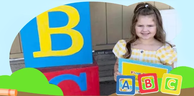 a little girl is holding a book in front of a stack of alphabet blocks