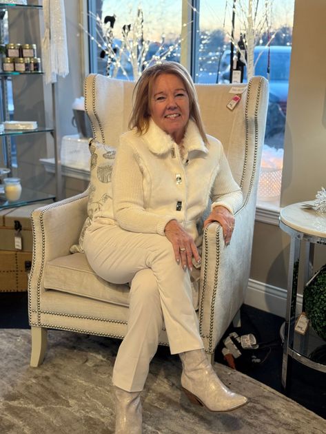 Woman smiling in a cream chair, wearing a white sweater in a bright indoor setting