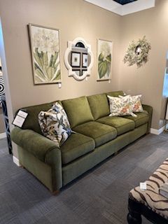 Green velvet sofa with decorative pillows in a showroom, beneath art and a mirror.