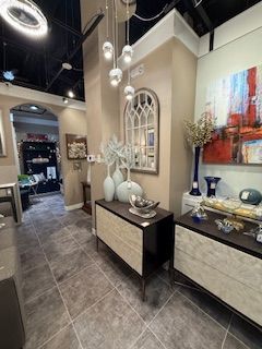 A living room with a dresser , mirror , vases and paintings on the wall.