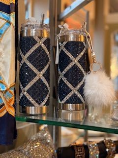 Two stainless steel tumblers with straws are sitting on a glass shelf.