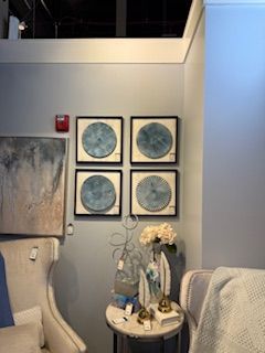 A living room with a couch , chair , table and paintings on the wall.