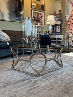 A glass coffee table is sitting on a rug in a living room.