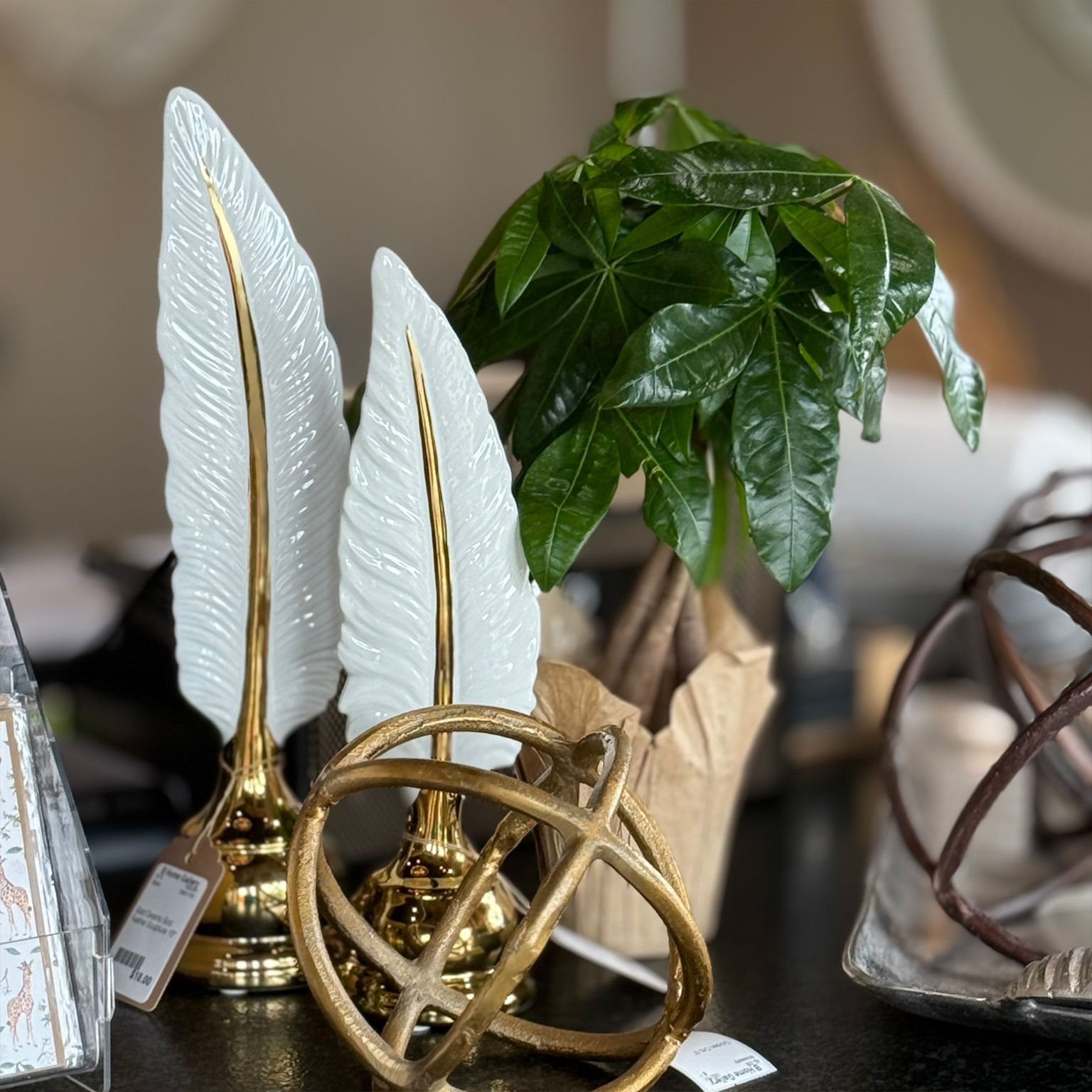 Close-up of decorative items: Two white and gold feather sculptures, a potted plant, and a gold orb.