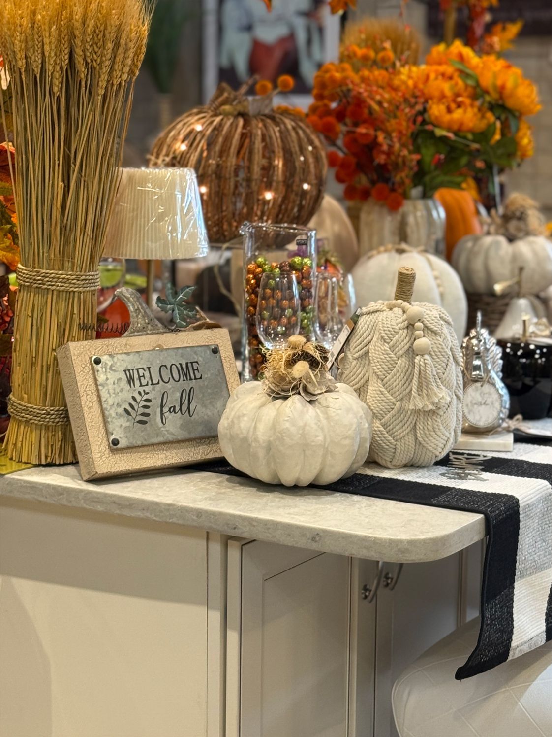 Fall-themed decor: pumpkins, flowers, and a 'Welcome Fall' sign displayed on a counter.