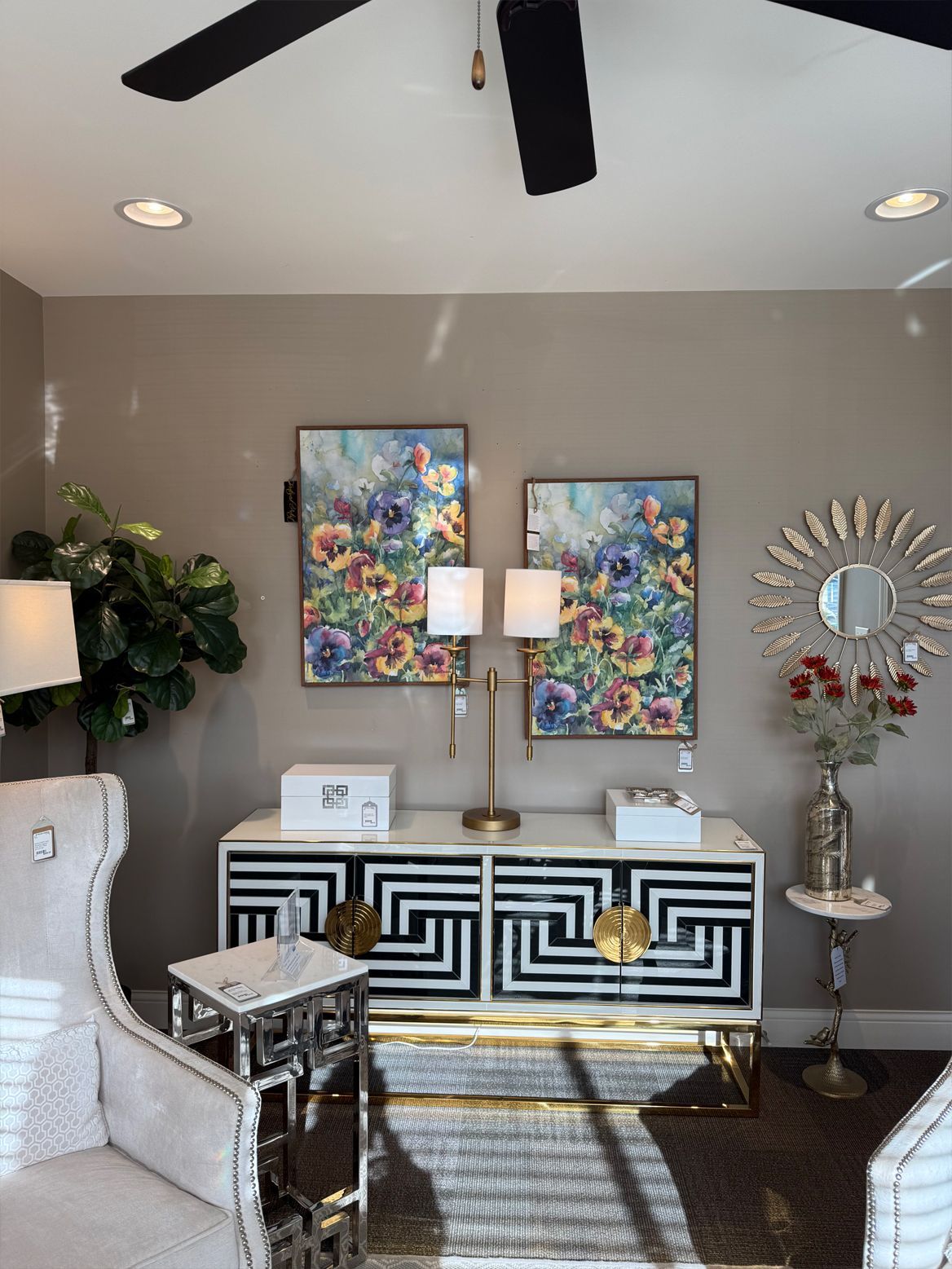 A stylish room featuring a black and white cabinet, floral art, a decorative mirror, and a table lamp.