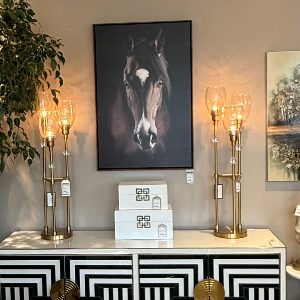 A room with a cabinet, lamps, and a horse portrait. Two gold lamps flank the portrait above white boxes.