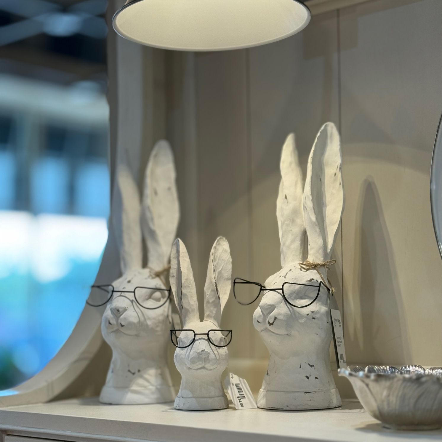 Three white rabbit sculptures with glasses on a shelf.