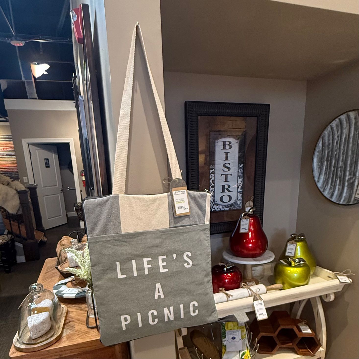 Gray tote bag with 'LIFE'S A PICNIC' text, hanging in a store.